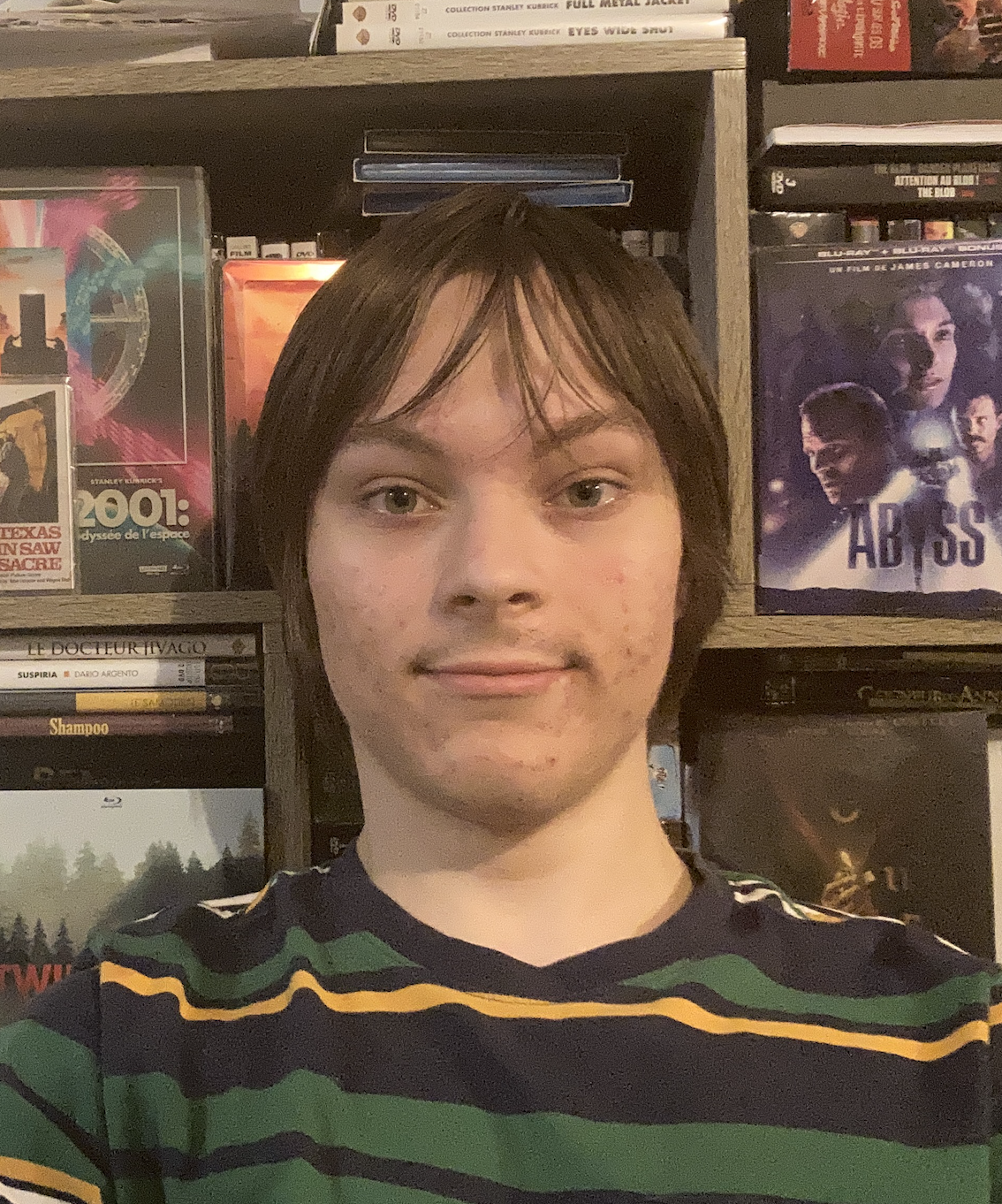 Mon Portrait. Dans la photo je suis en train de sourire et derrière moi se trouve une étagère de DVD.