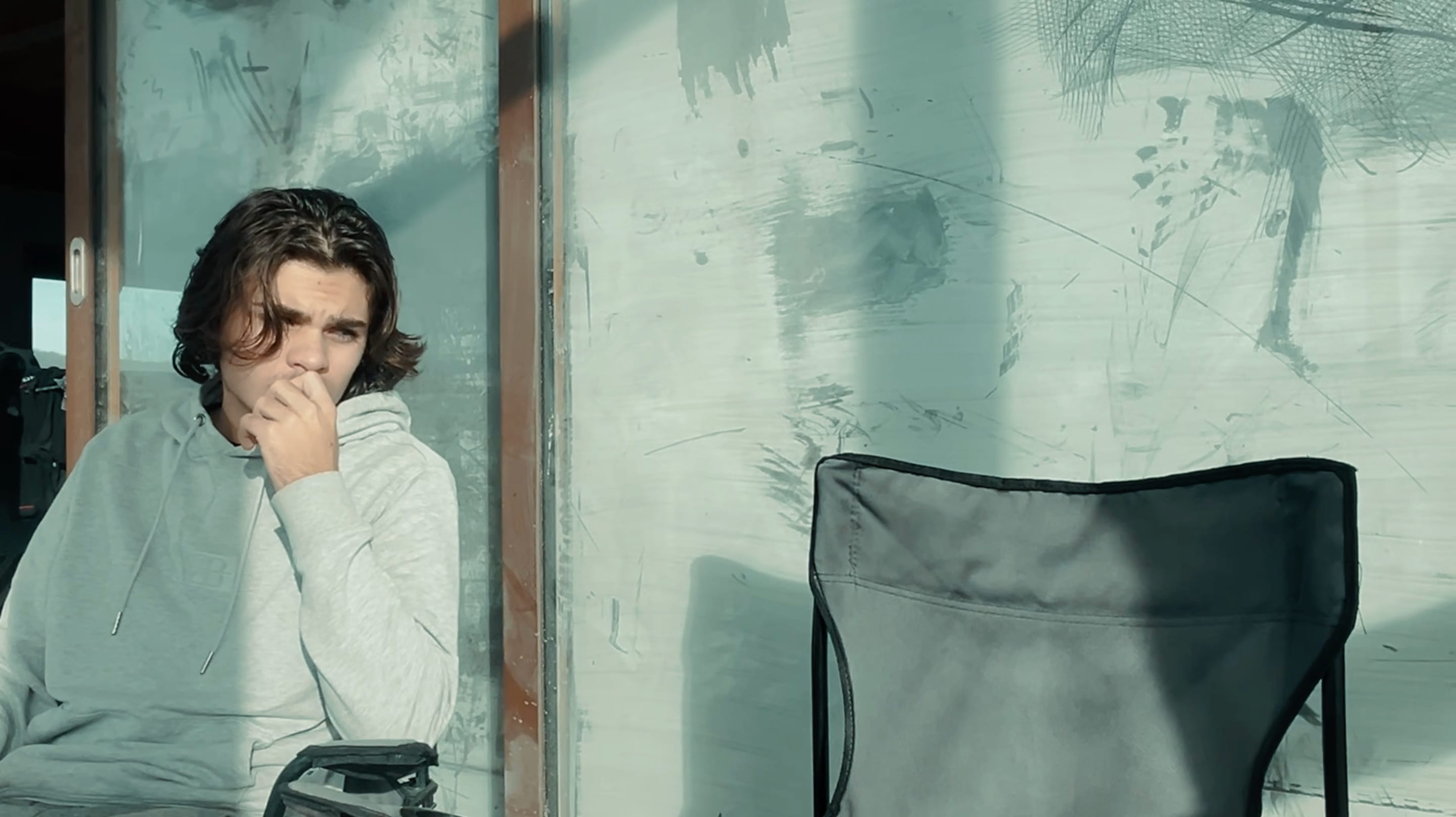 3e photographie d'Anemoia où un homme regarde le fauteuil vide qui se trouve à sa gauche. Derrière lui se trouvent de grandes fenêtres coulissantes qui sont recouvertes de blanc de Meudon.